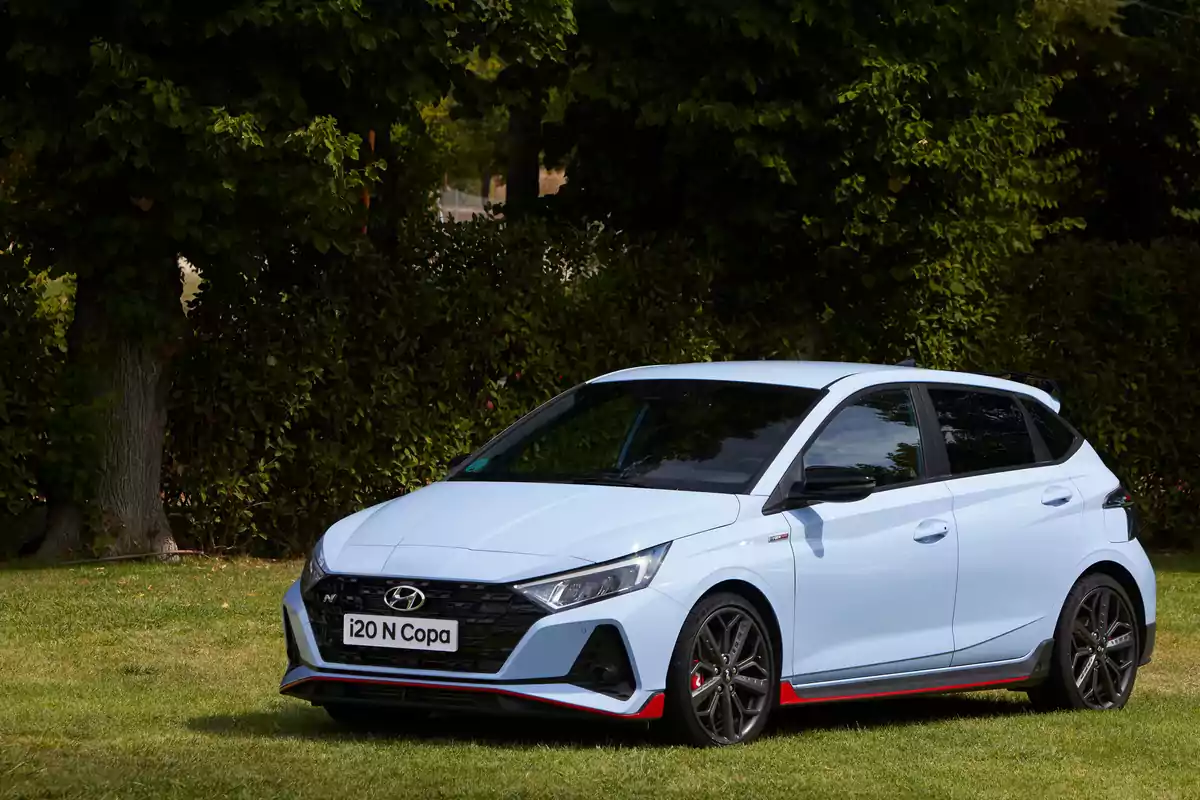 Un coche Hyundai i20 N Copa de color azul claro estacionado en un área verde con árboles y arbustos al fondo.