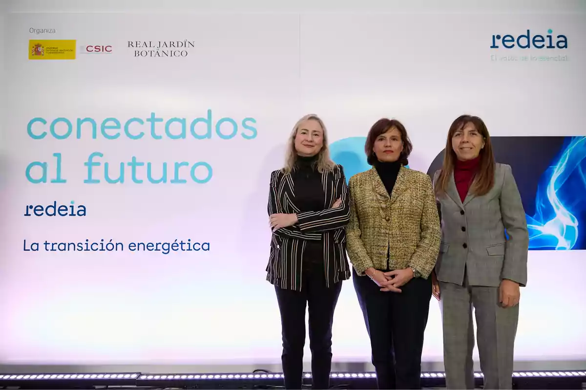 Tres mujeres posan frente a un cartel que dice "conectados al futuro" en un evento sobre la transición energética organizado por el CSIC y el Real Jardín Botánico.