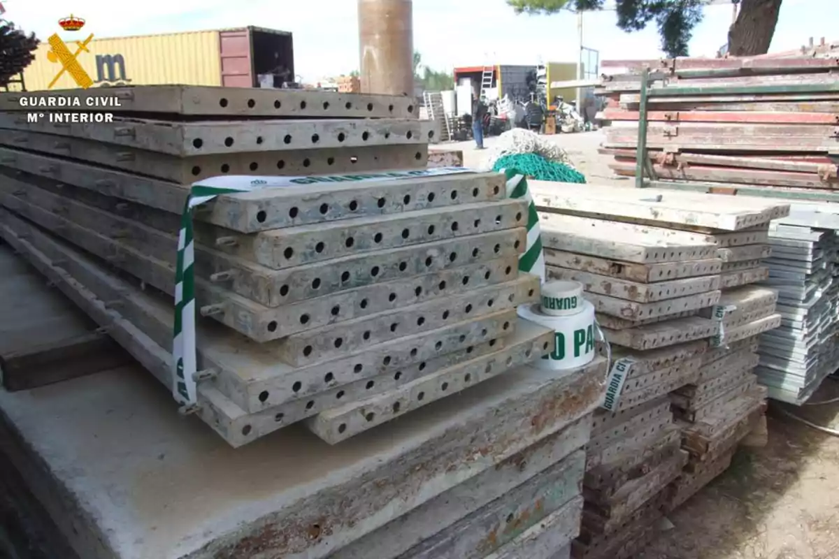 Una pila de tablones de construcción apilados en un sitio de trabajo, con una cinta de la Guardia Civil alrededor.
