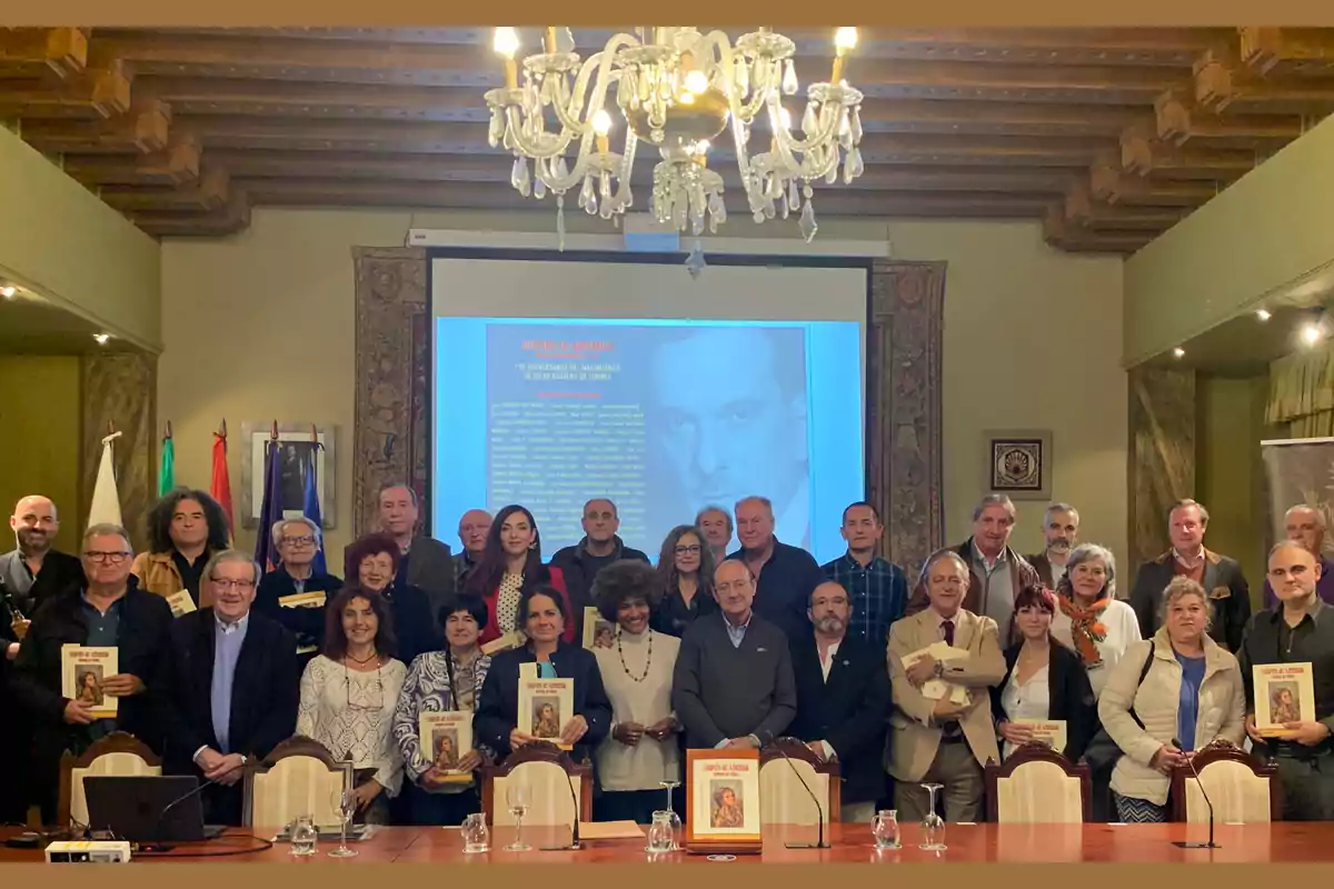 Un grupo de personas posando en una sala con un candelabro y una pantalla de proyección al fondo.