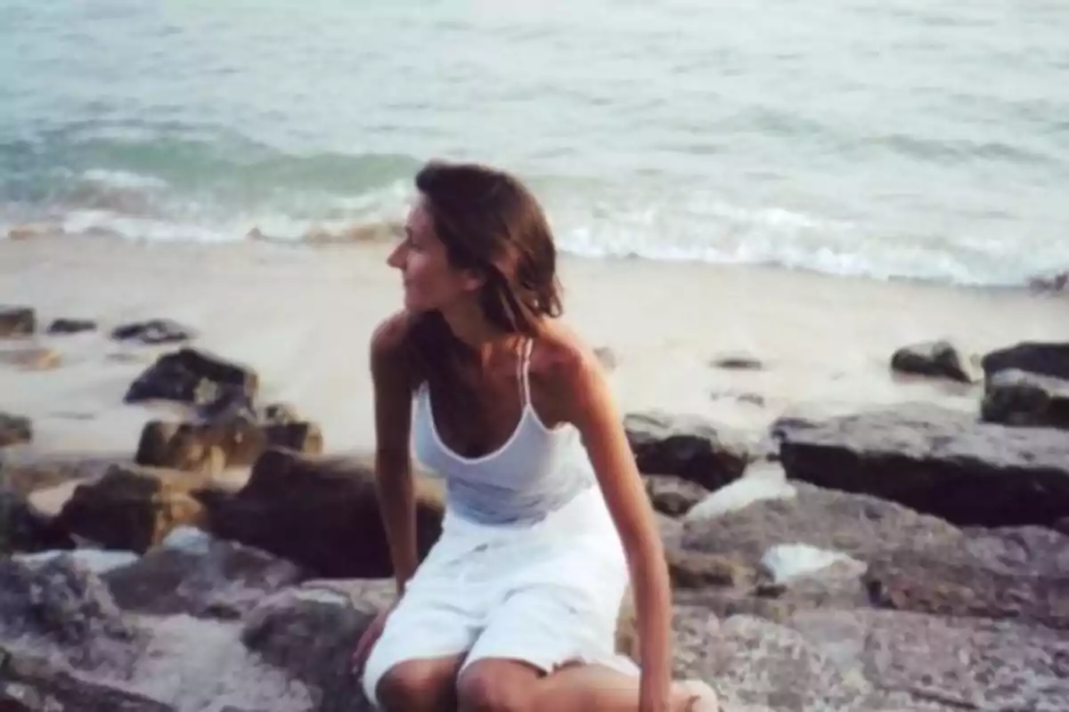 Una mujer sentada en unas rocas junto al mar, mirando hacia la derecha.