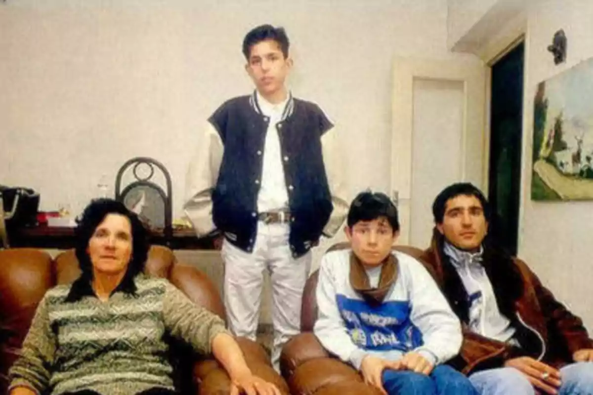 Una familia sentada en un sofá con un joven de pie detrás de ellos en una sala de estar.