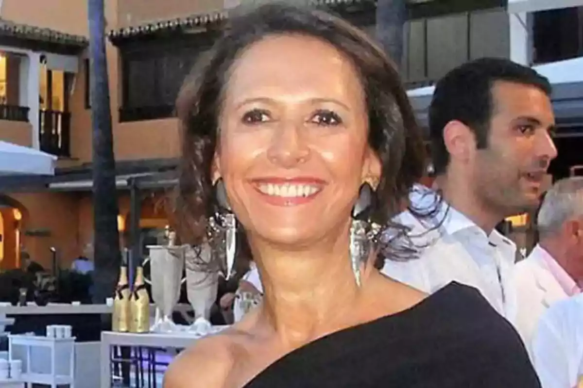 Una mujer sonriente con un vestido negro y grandes pendientes plateados en un evento al aire libre.