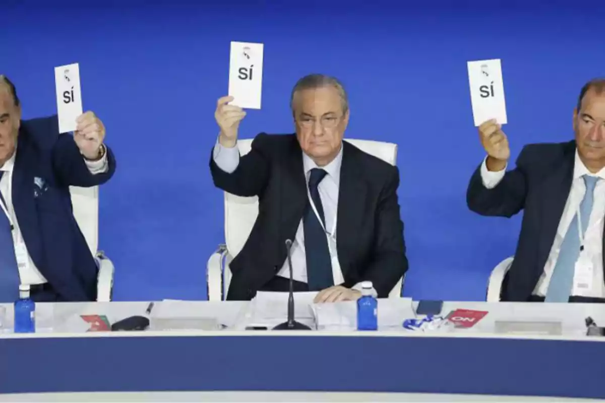 Tres hombres en trajes formales levantan tarjetas con la palabra "sí" en un evento.