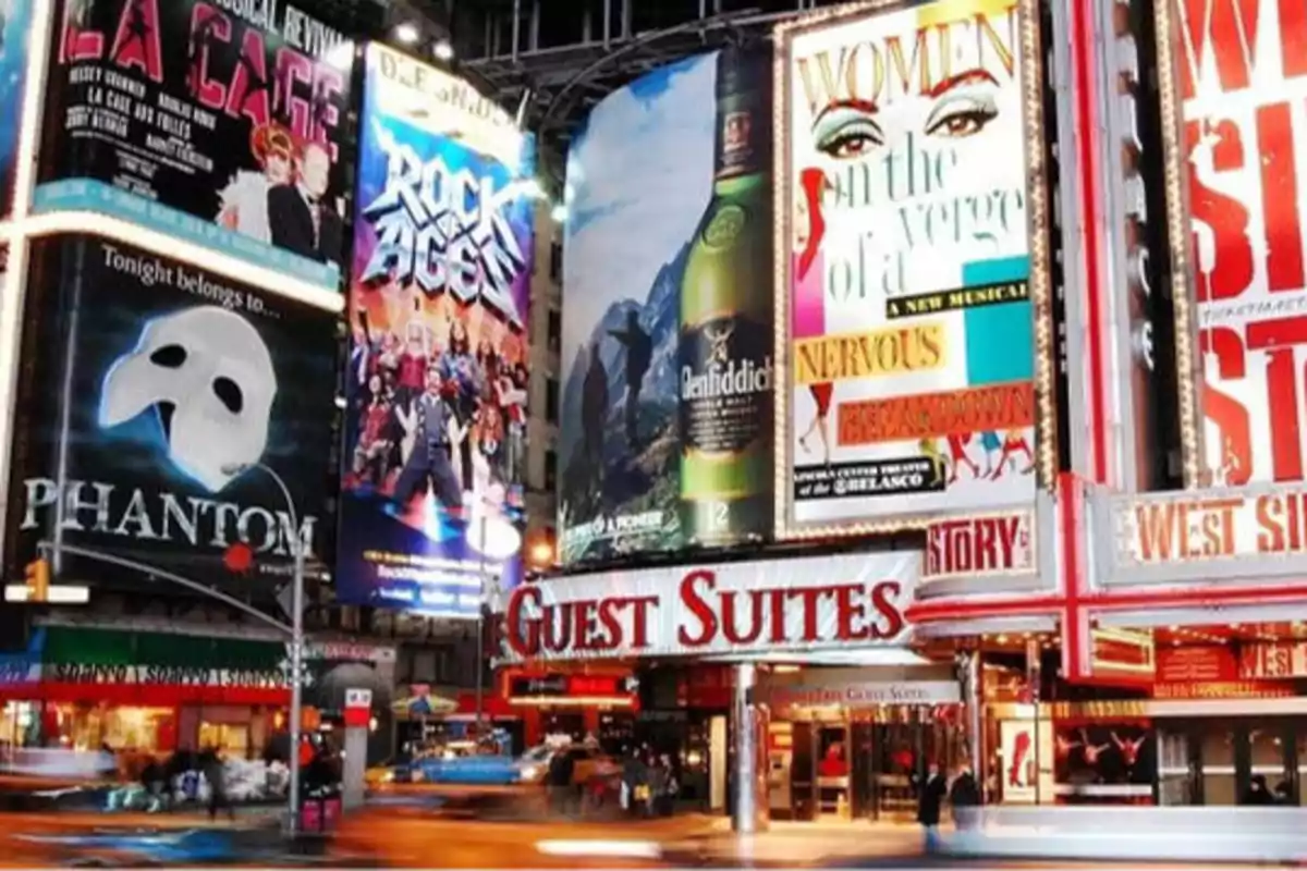 Carteles luminosos de Broadway en una calle concurrida con anuncios de musicales y obras de teatro.