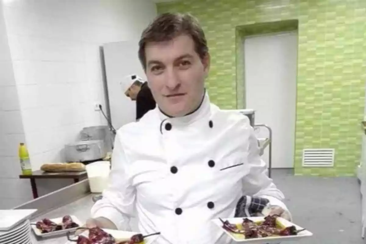 Un chef con uniforme blanco sosteniendo dos platos de comida en una cocina.