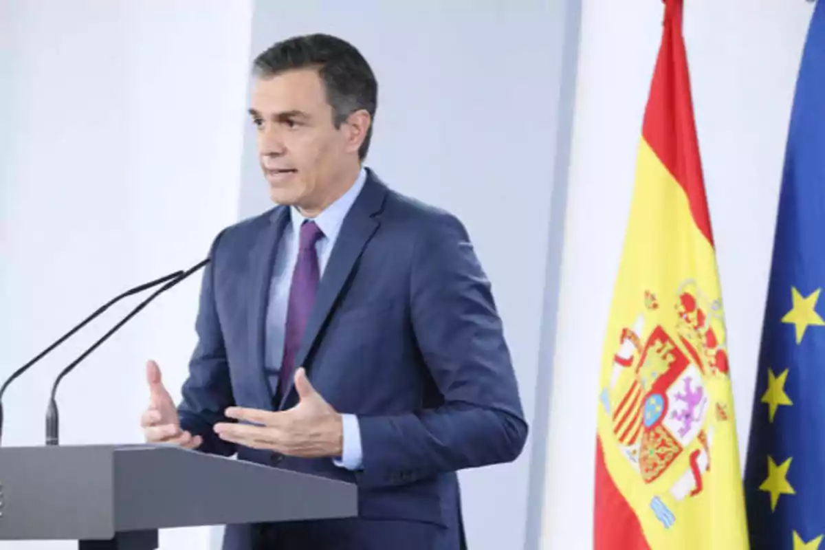 Hombre de traje dando un discurso frente a un podio con las banderas de España y la Unión Europea en el fondo.