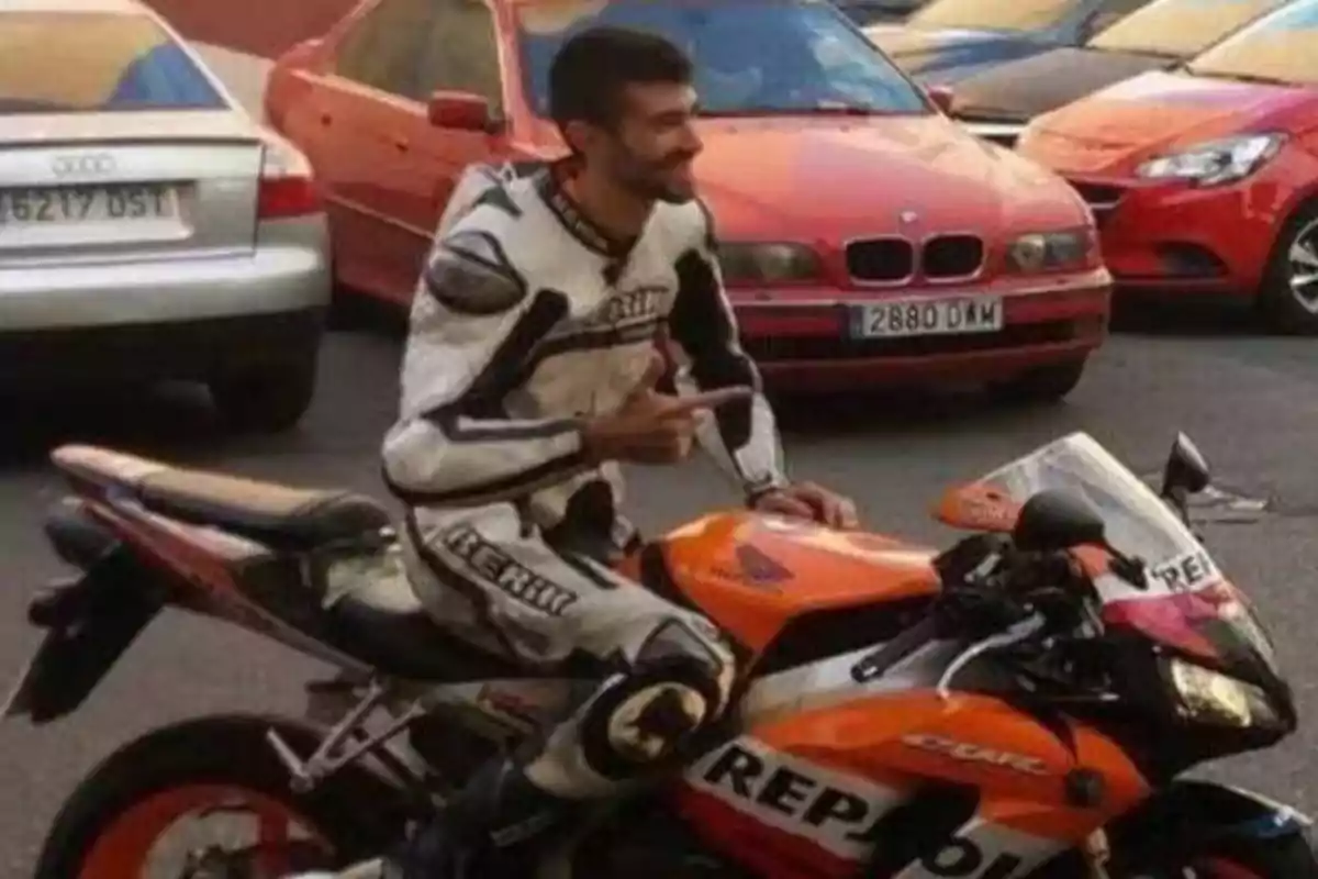 Un hombre con traje de motociclista está sentado en una motocicleta Repsol en un estacionamiento, rodeado de varios coches.