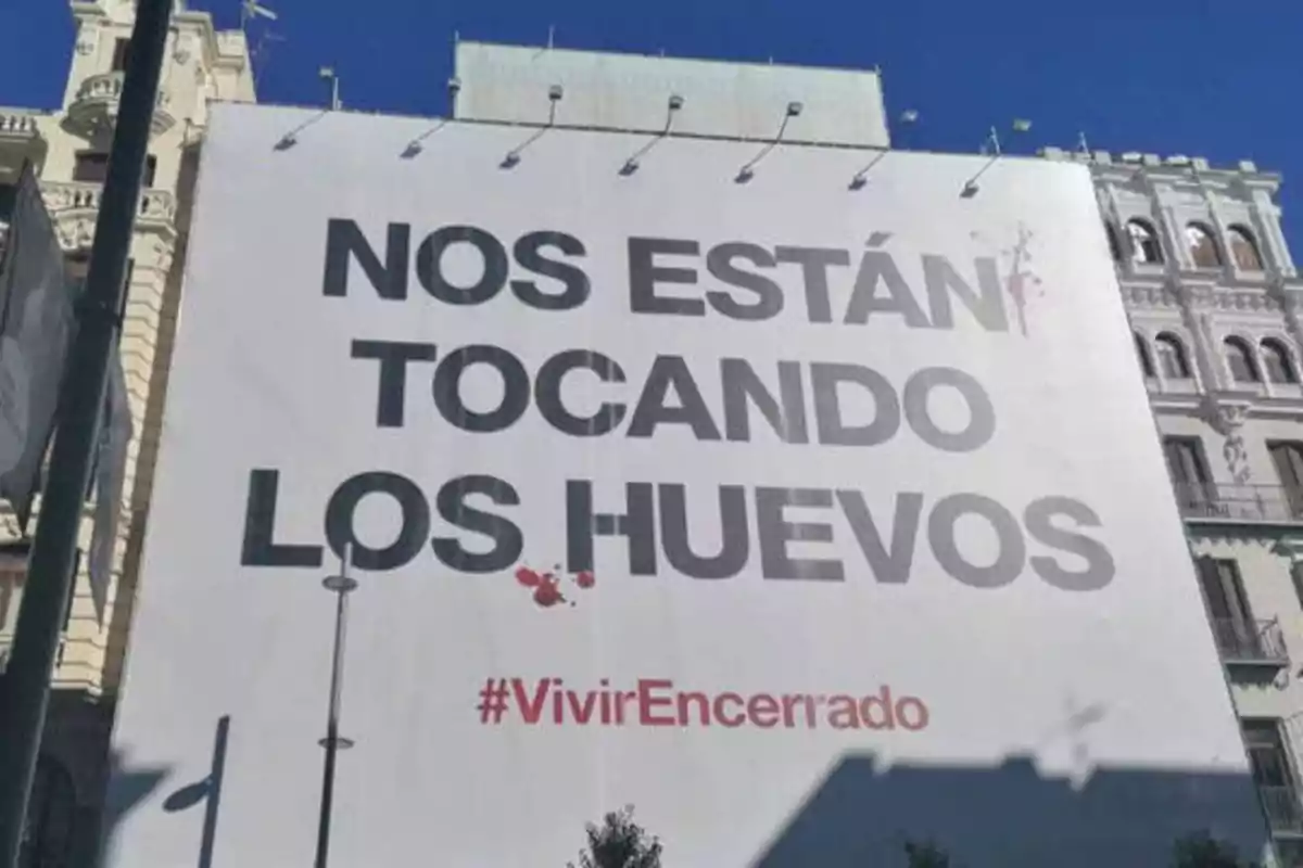 Un cartel en una ciudad con el mensaje "NOS ESTÁN TOCANDO LOS HUEVOS" y el hashtag "#VivirEncerrado".