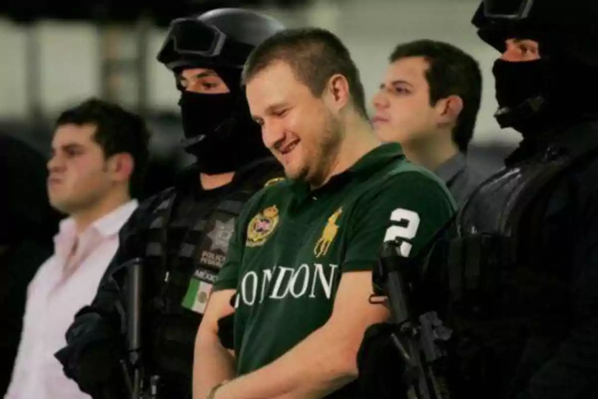 Un hombre con una camiseta verde es escoltado por oficiales de policía enmascarados.