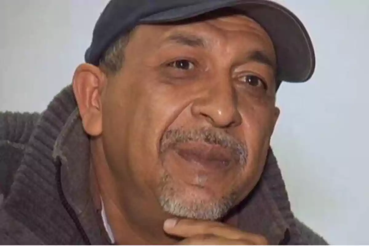 Un hombre con barba y bigote, usando una gorra y un suéter, mira pensativamente hacia adelante.