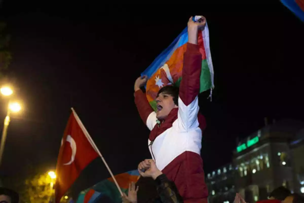 Persona celebrando con una bandera de Azerbaiyán en la noche, rodeada de otras personas y banderas.