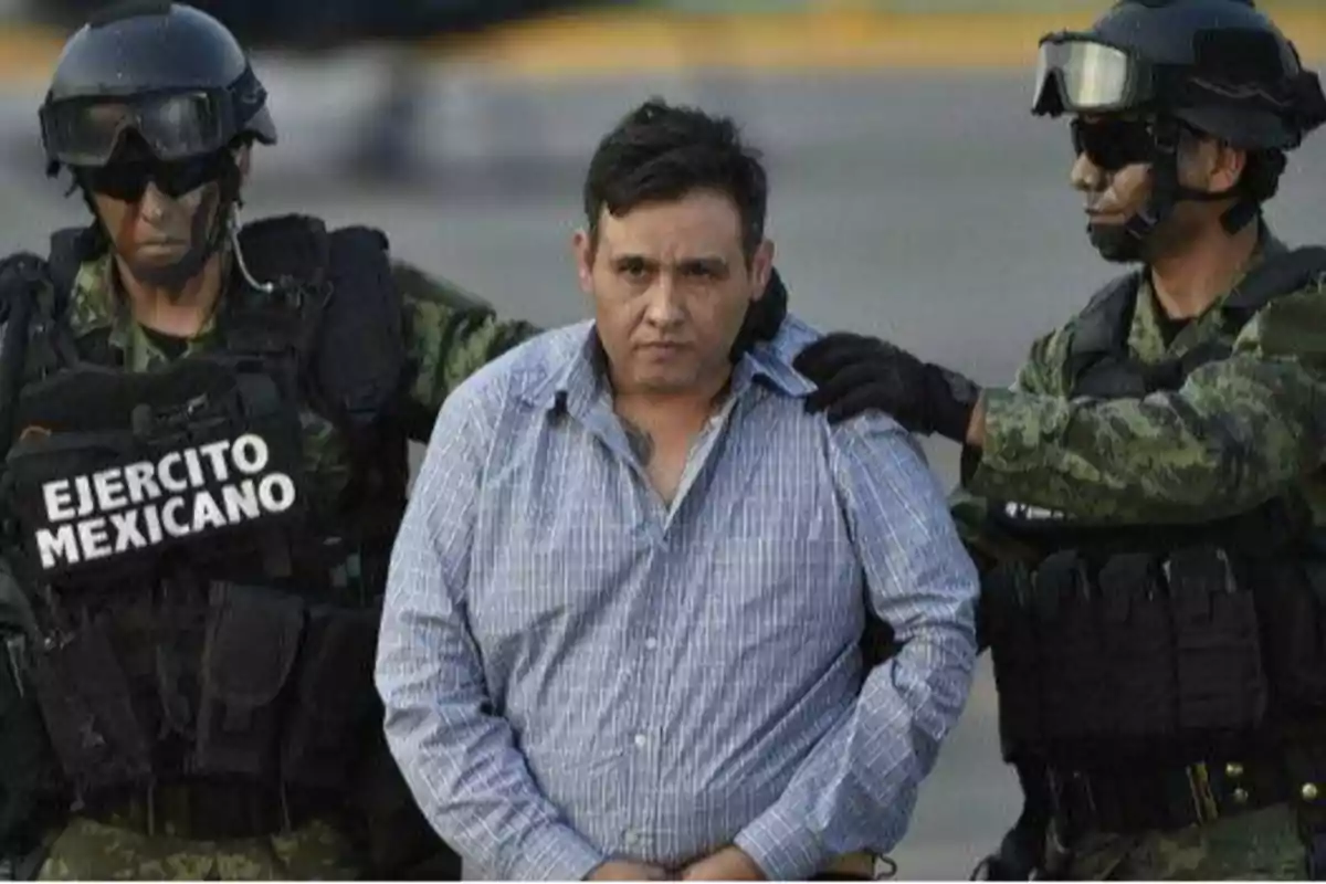 Un hombre con camisa a cuadros es escoltado por dos soldados del Ejército Mexicano que llevan equipo táctico y cascos.