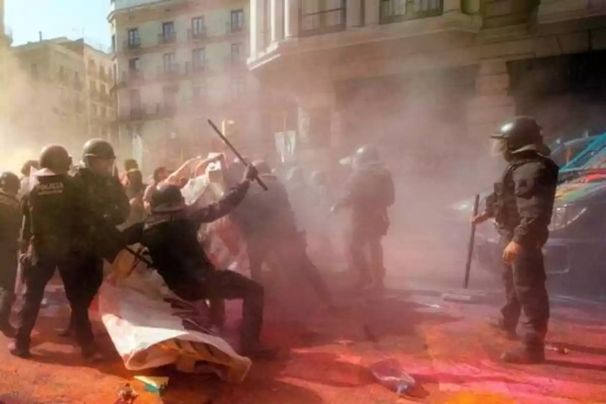 Policías antidisturbios enfrentándose a manifestantes en una calle llena de humo y polvo.