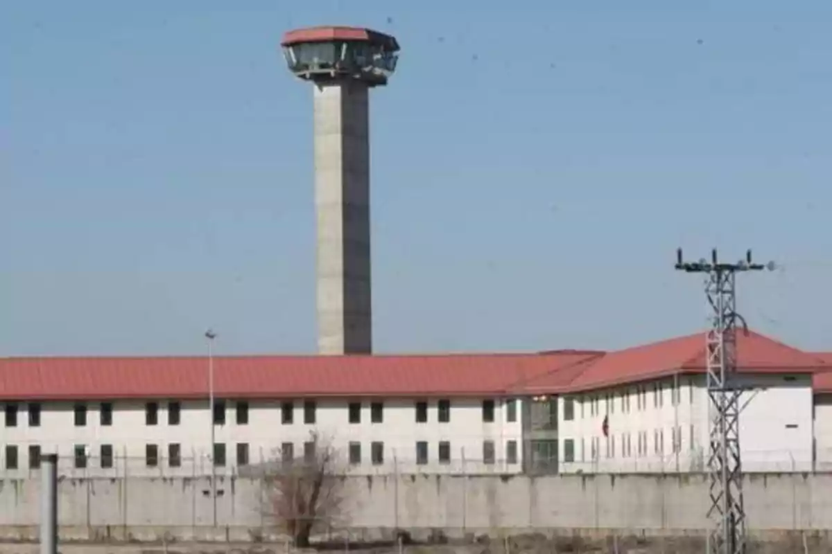 Edificio con techo rojo y una torre de vigilancia alta en un entorno cerrado.