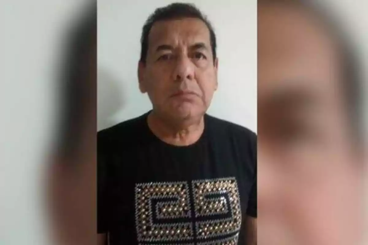 Hombre de mediana edad con cabello corto y oscuro, vistiendo una camiseta negra con un diseño geométrico en la parte frontal, posando frente a una pared blanca.