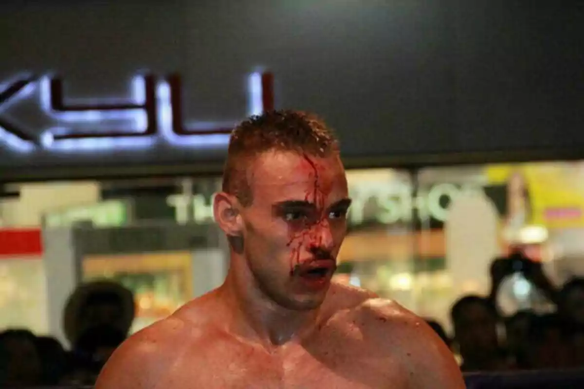 Un luchador con el rostro ensangrentado durante una pelea, con un fondo borroso que muestra un letrero iluminado.