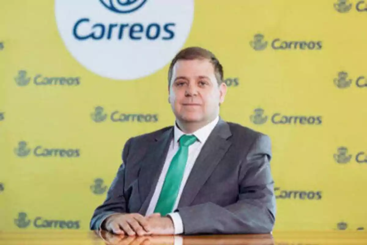 Hombre con traje y corbata verde sentado frente a un fondo amarillo con el logo de Correos.