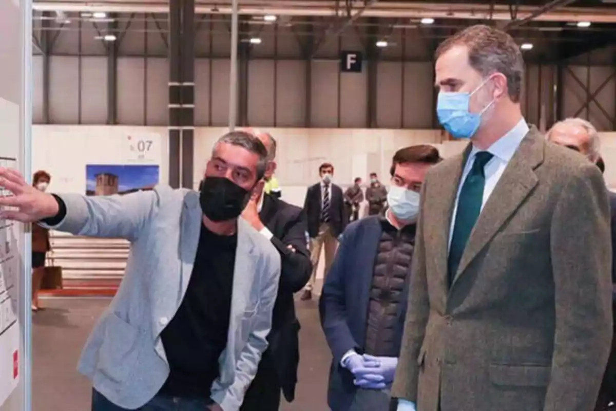 Un grupo de personas con mascarillas observa una presentación en un recinto cerrado.