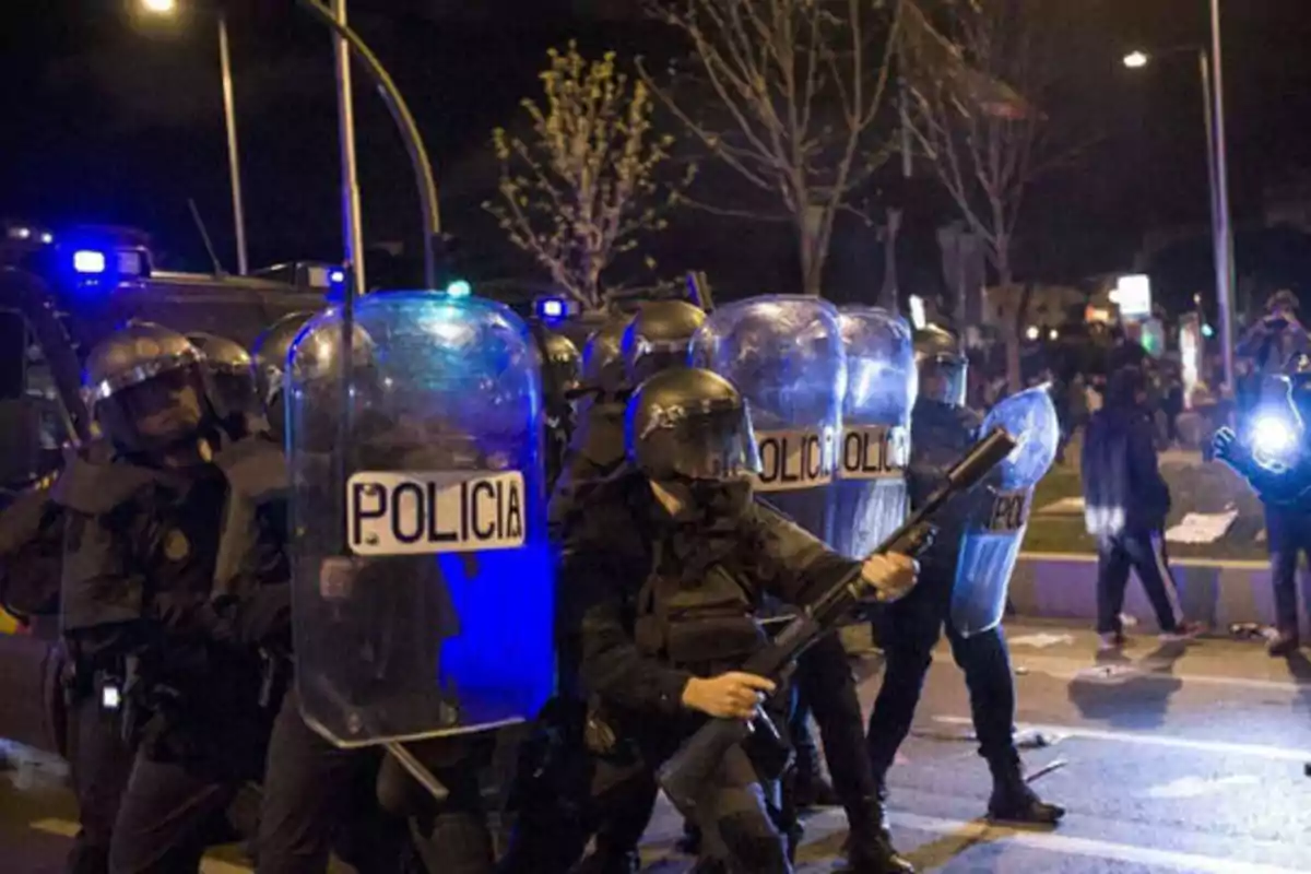 Policías antidisturbios con escudos y cascos en una manifestación nocturna.