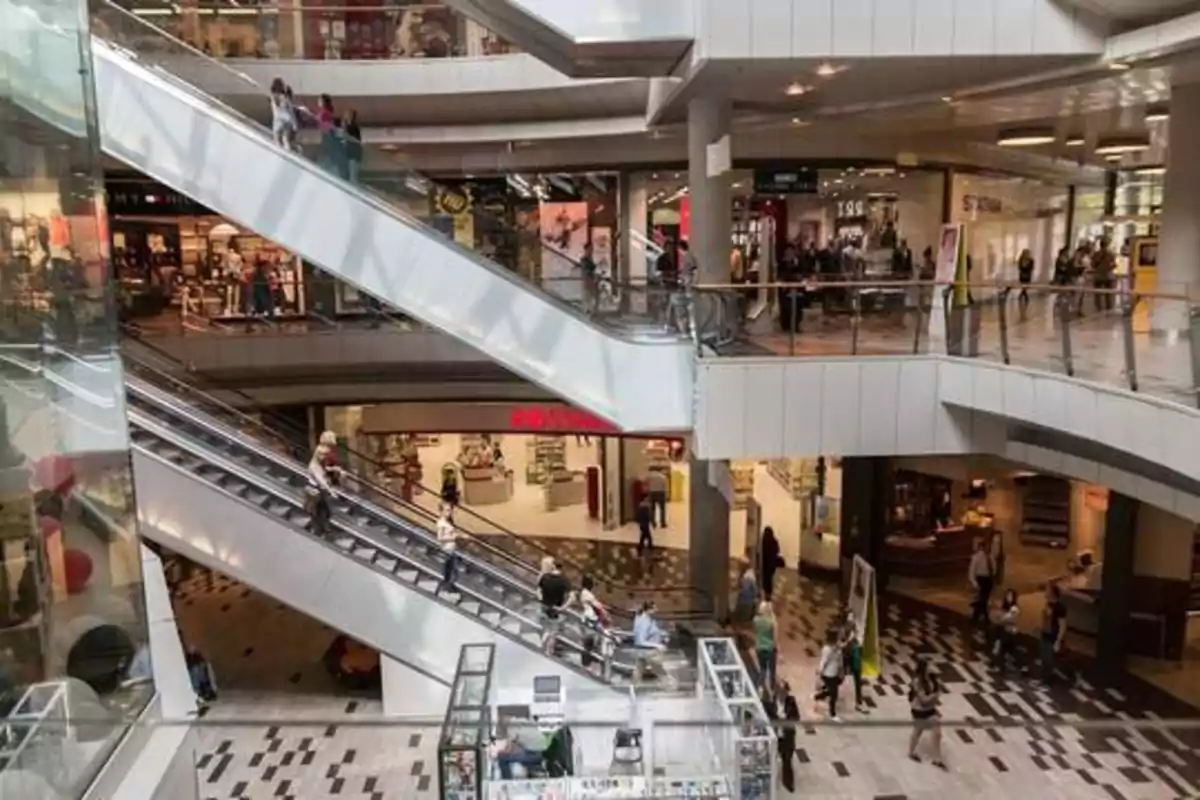 Centro comercial con varias plantas, escaleras mecánicas y personas caminando y comprando.