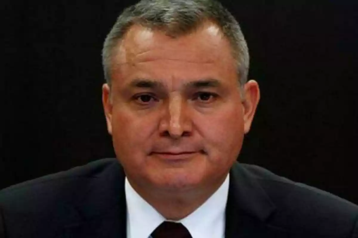 Hombre de mediana edad con cabello corto y canoso, vestido con traje oscuro y corbata, sobre un fondo negro.