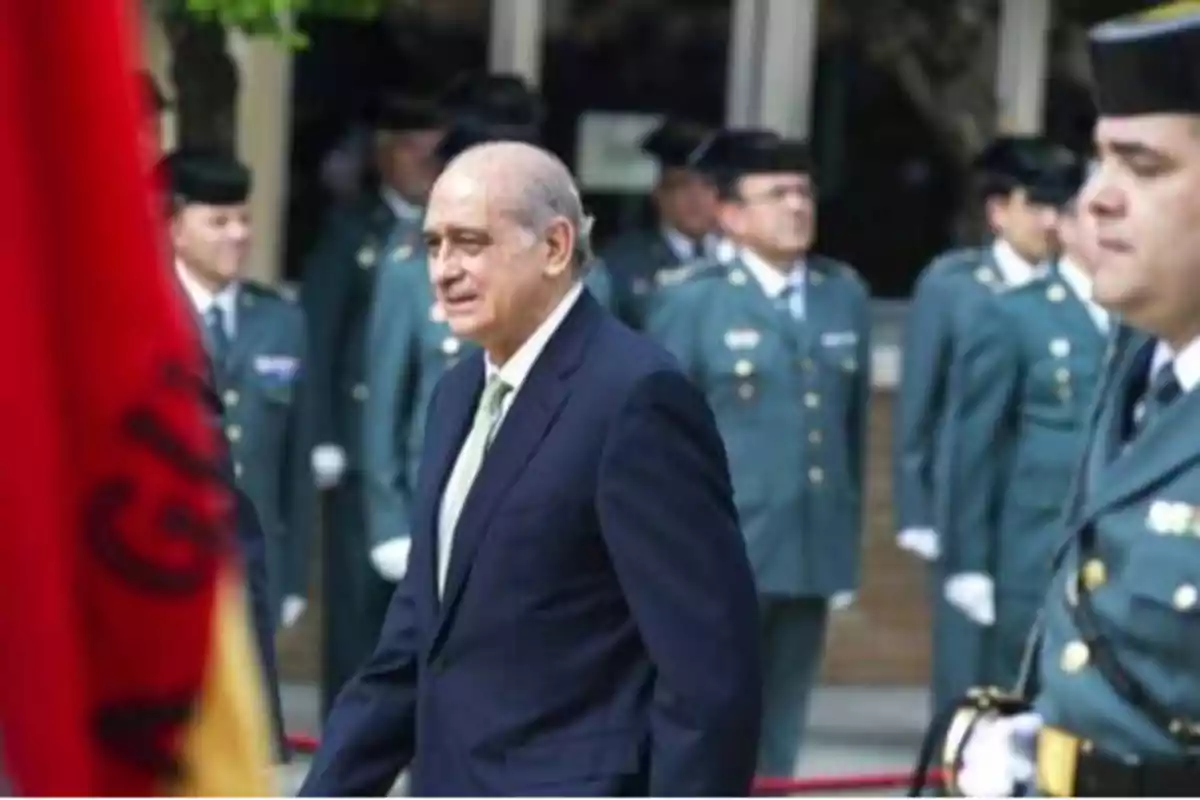 Un hombre de traje oscuro y corbata clara camina frente a un grupo de oficiales uniformados.