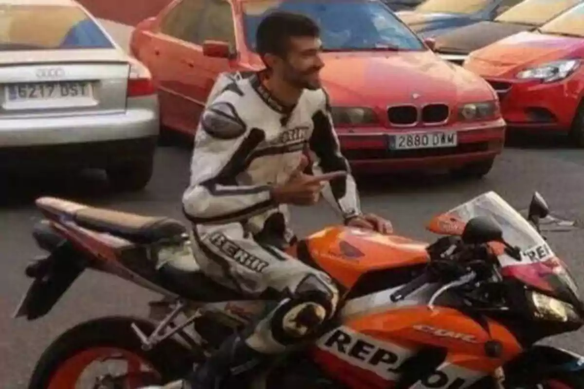 Un hombre con traje de motociclista está sentado en una motocicleta Repsol Honda CBR en un estacionamiento, haciendo un gesto con la mano.