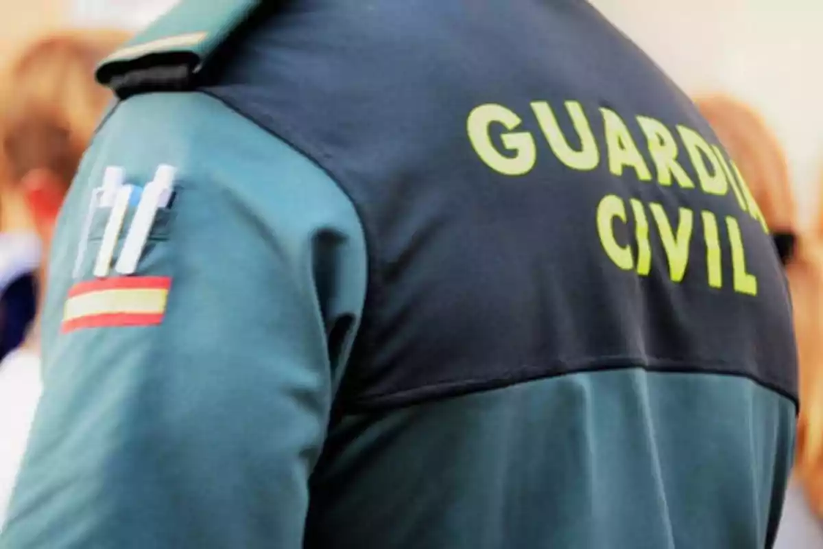 Un agente de la Guardia Civil con uniforme verde y negro, con la bandera de España en la manga y bolígrafos en el bolsillo.
