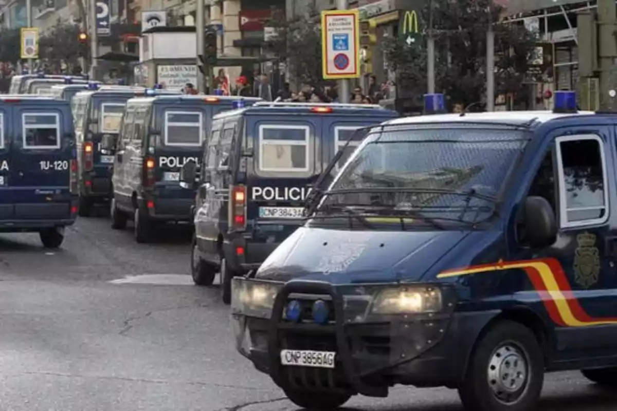 Una fila de furgonetas de la policía circula por una calle urbana.