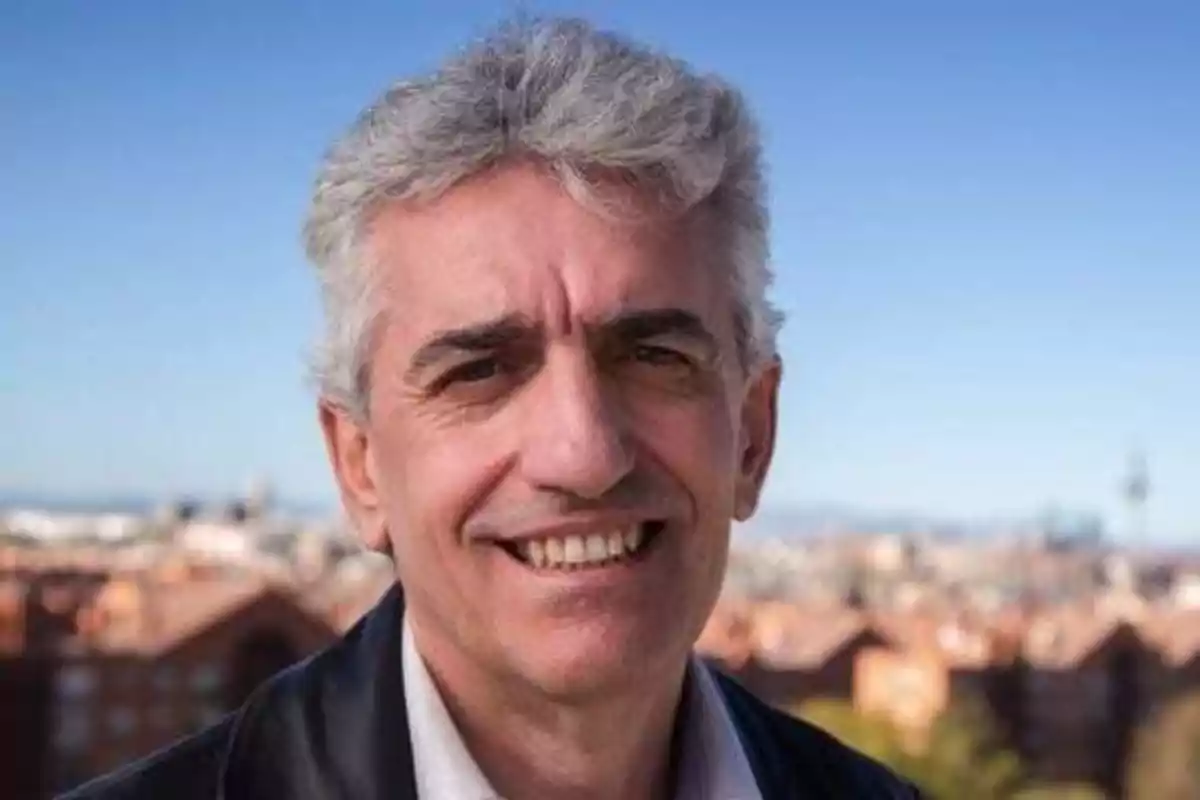 Hombre de cabello canoso sonriendo al aire libre con una ciudad desenfocada de fondo.