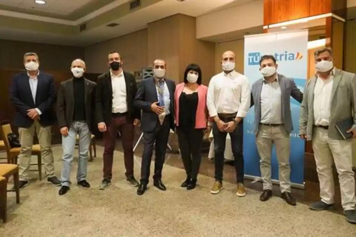 Un grupo de personas con mascarillas posando para una foto en un entorno interior, con un cartel de fondo que dice "TUristria".