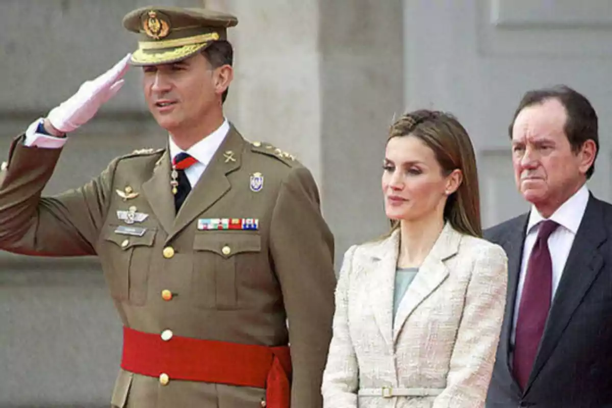 Un oficial militar saluda mientras está acompañado por una mujer y un hombre en un evento formal.