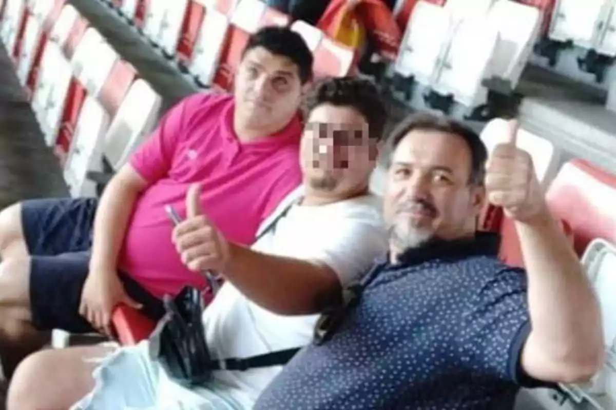 Tres hombres sentados en las gradas de un estadio, dos de ellos levantando el pulgar.