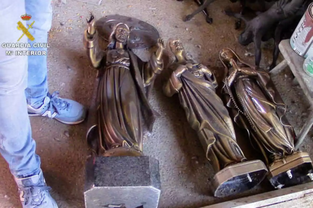 Estatuas religiosas de bronce tumbadas en el suelo junto a una persona con jeans y zapatillas deportivas.