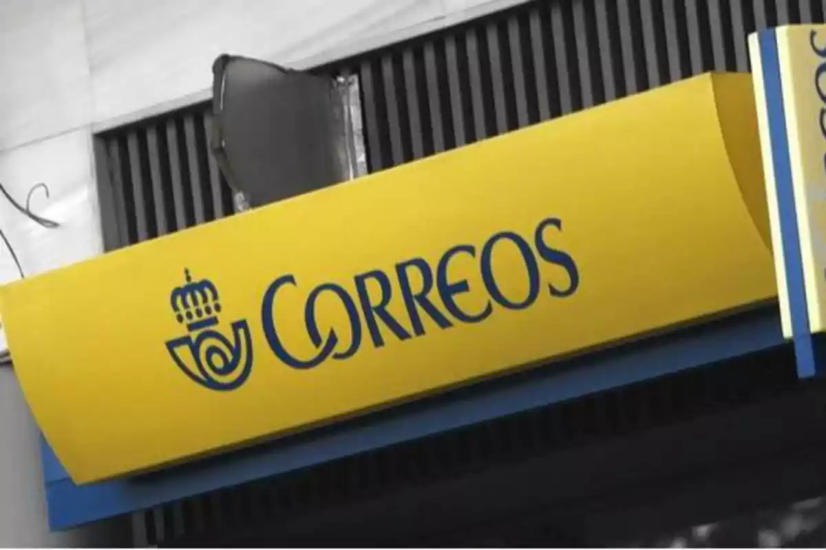 Letrero amarillo de Correos con letras azules y logotipo en la fachada de un edificio.