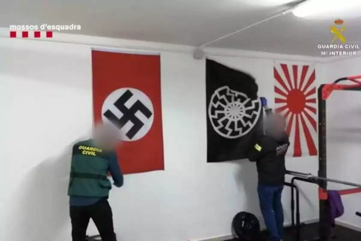 Agentes de la Guardia Civil y Mossos d'Esquadra inspeccionan una habitación con banderas de simbología nazi y de extrema derecha.