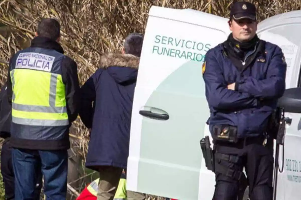 Policías y personal de servicios funerarios en una escena al aire libre.