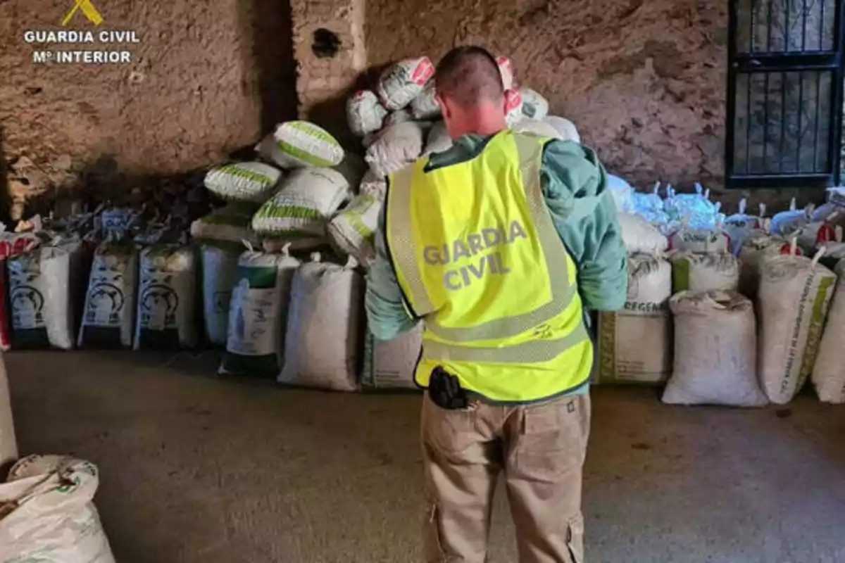 Un agente de la Guardia Civil inspecciona un almacén lleno de sacos.