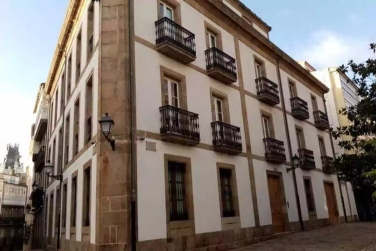 Edificio de tres pisos con fachada blanca y detalles en piedra, con balcones de hierro forjado y farolas en la calle.