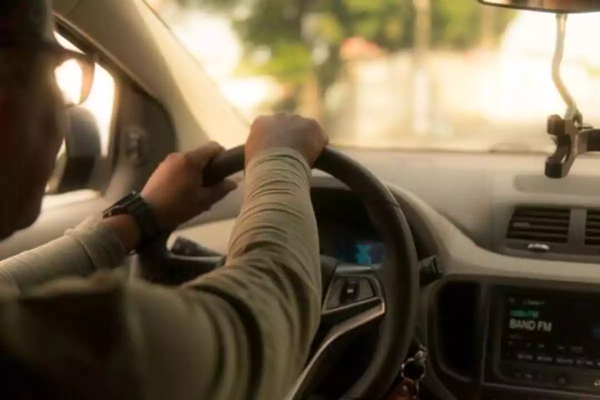 Persona conduciendo un automóvil con ambas manos en el volante y el tablero del vehículo visible.
