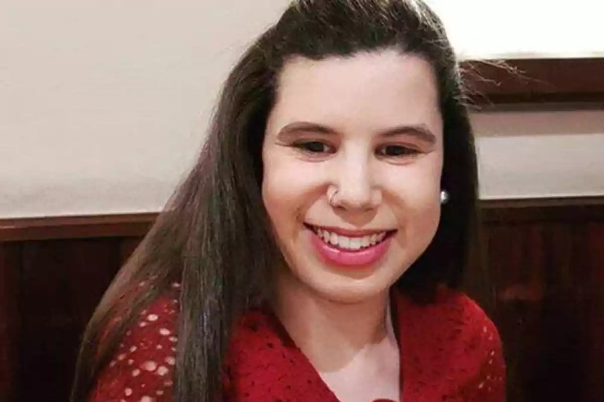 Una mujer con cabello largo y lacio, sonriendo y usando una blusa roja.