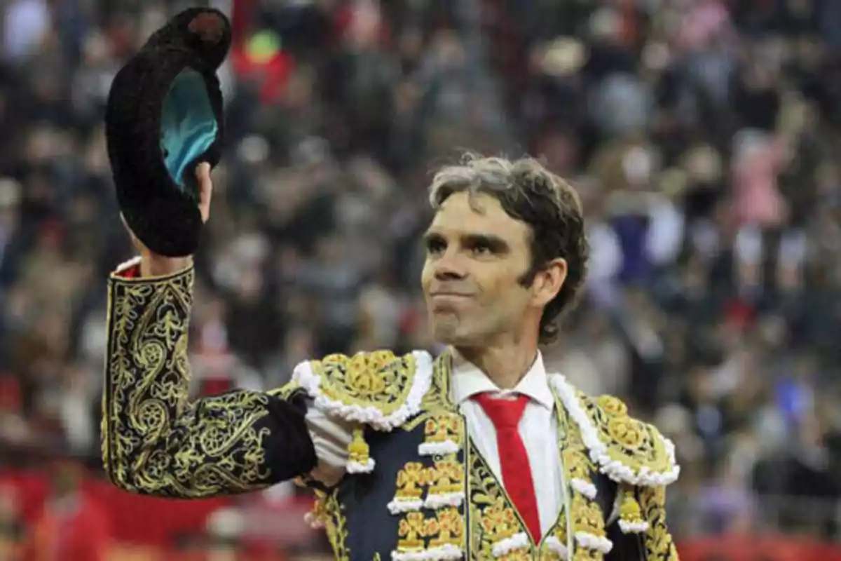 Un torero vestido con traje de luces levanta su montera en una plaza de toros llena de espectadores.