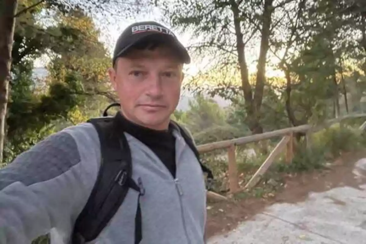 Un hombre con gorra y mochila se toma una selfie en un sendero rodeado de árboles y vegetación.