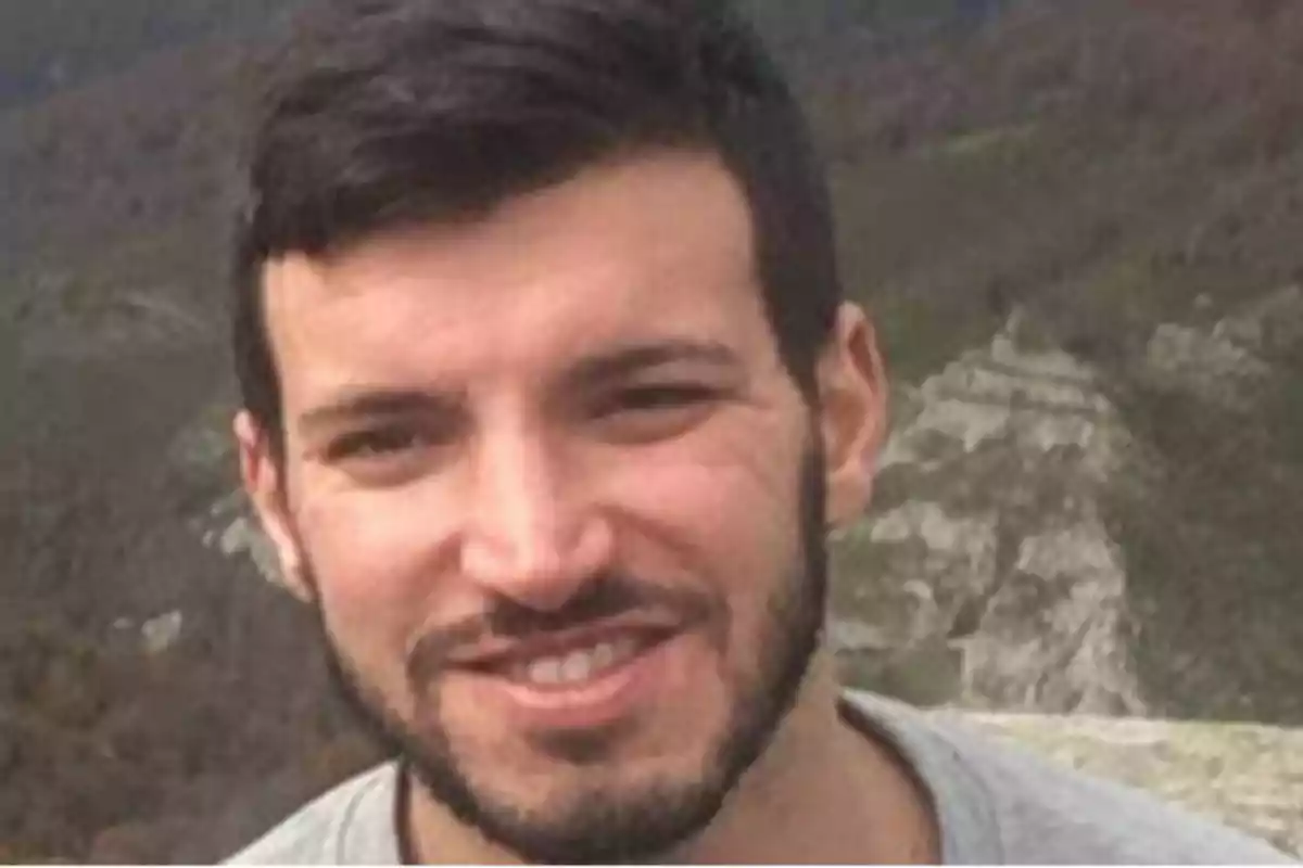 Hombre con barba sonriendo al aire libre con un paisaje montañoso de fondo.