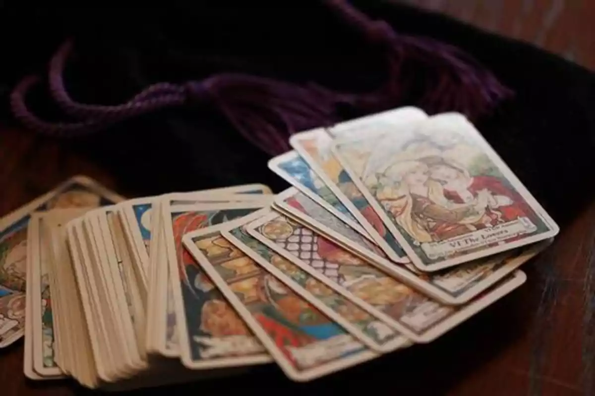 Una baraja de cartas de tarot extendida sobre una mesa con una bolsa de terciopelo negro y cordones morados en el fondo.