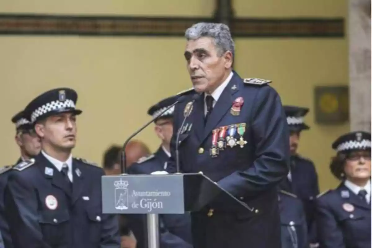 Un oficial de policía dando un discurso en un podio del Ayuntamiento de Gijón, acompañado por otros oficiales de policía.