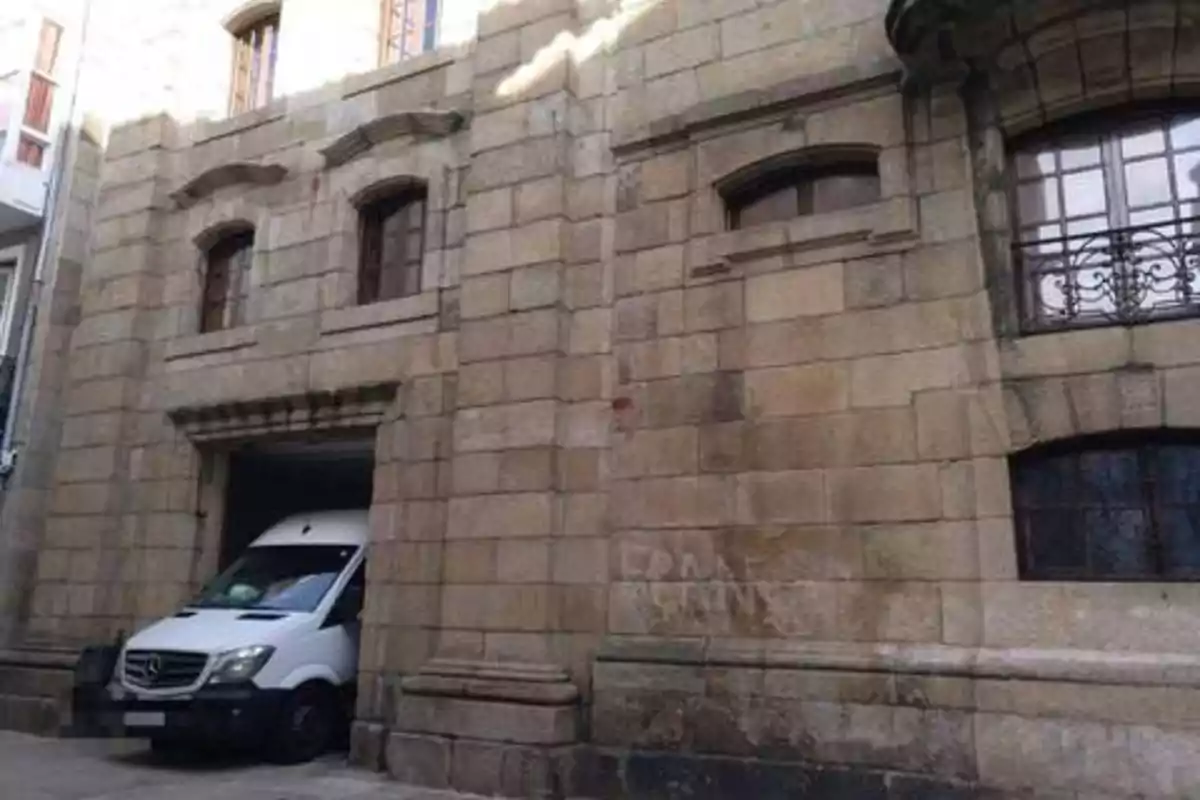 Una furgoneta blanca está parcialmente estacionada dentro de un edificio de piedra con ventanas de arco.