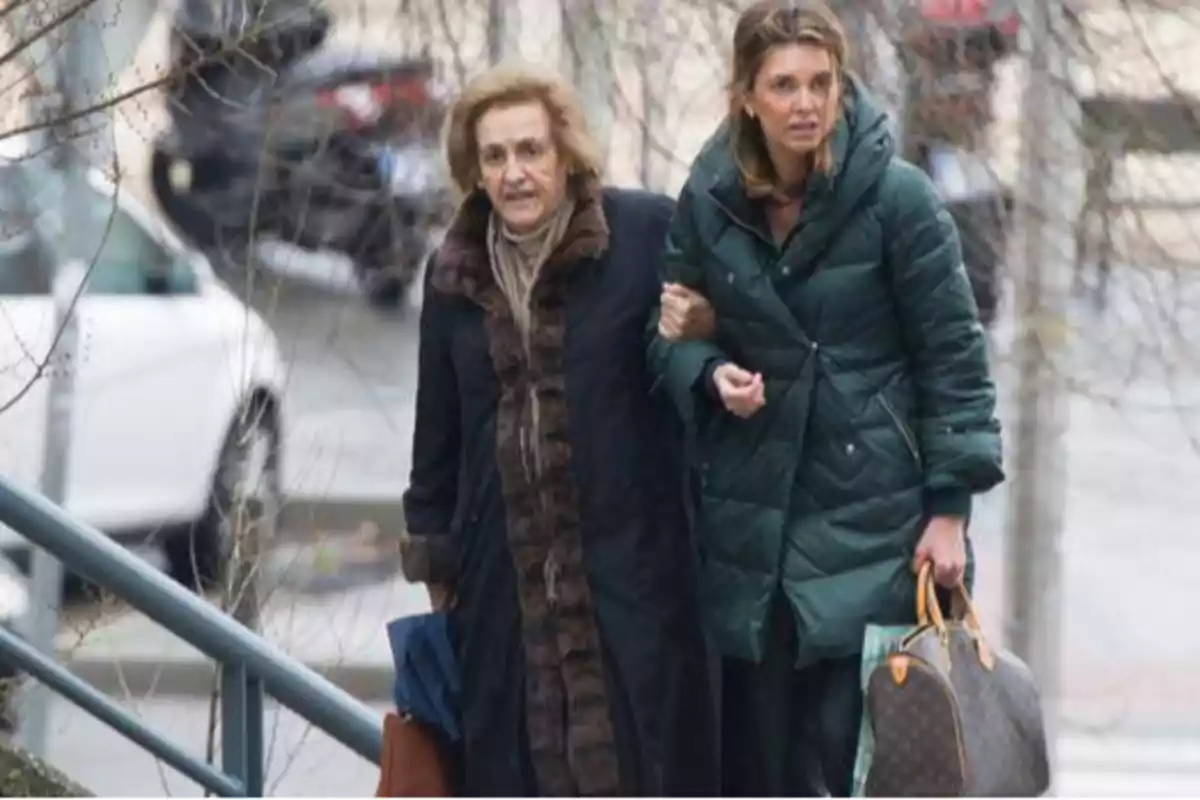 Dos mujeres caminando por la calle, una de ellas ayudando a la otra mientras ambas llevan abrigos gruesos y bolsas.