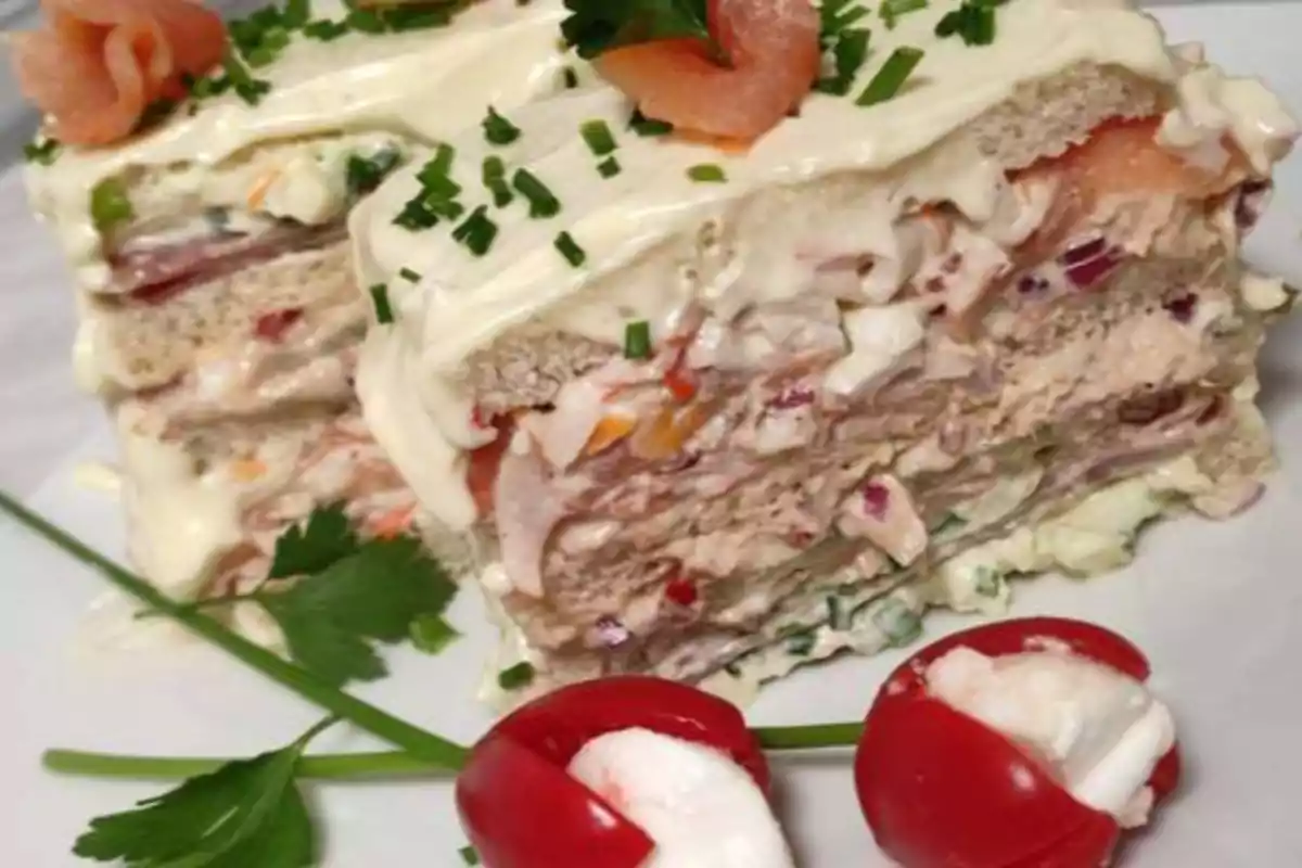 Un pastel de pan de molde relleno de ensalada de atún y decorado con mayonesa, cebollino y rodajas de salmón, acompañado de tomates cherry rellenos de queso crema y hojas de perejil.